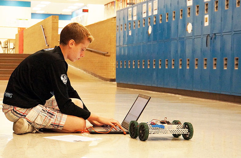 middle school student programming a robot on a laptop